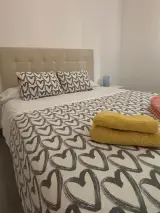Dormitorio doble desde la esquina con cabecero acolchado, colcha de corazones y cortinas de hojas